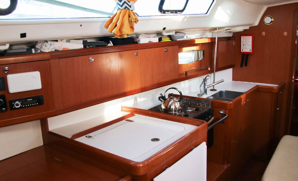cuisine d'un voilier type oceanis 40 de location avec une frigo glacière au premier plan. Ton de bois rouge, marron rouge.