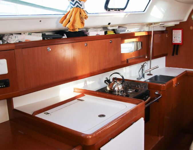 cuisine d'un voilier type oceanis 40 de location avec une frigo glacière au premier plan. Ton de bois rouge, marron rouge.