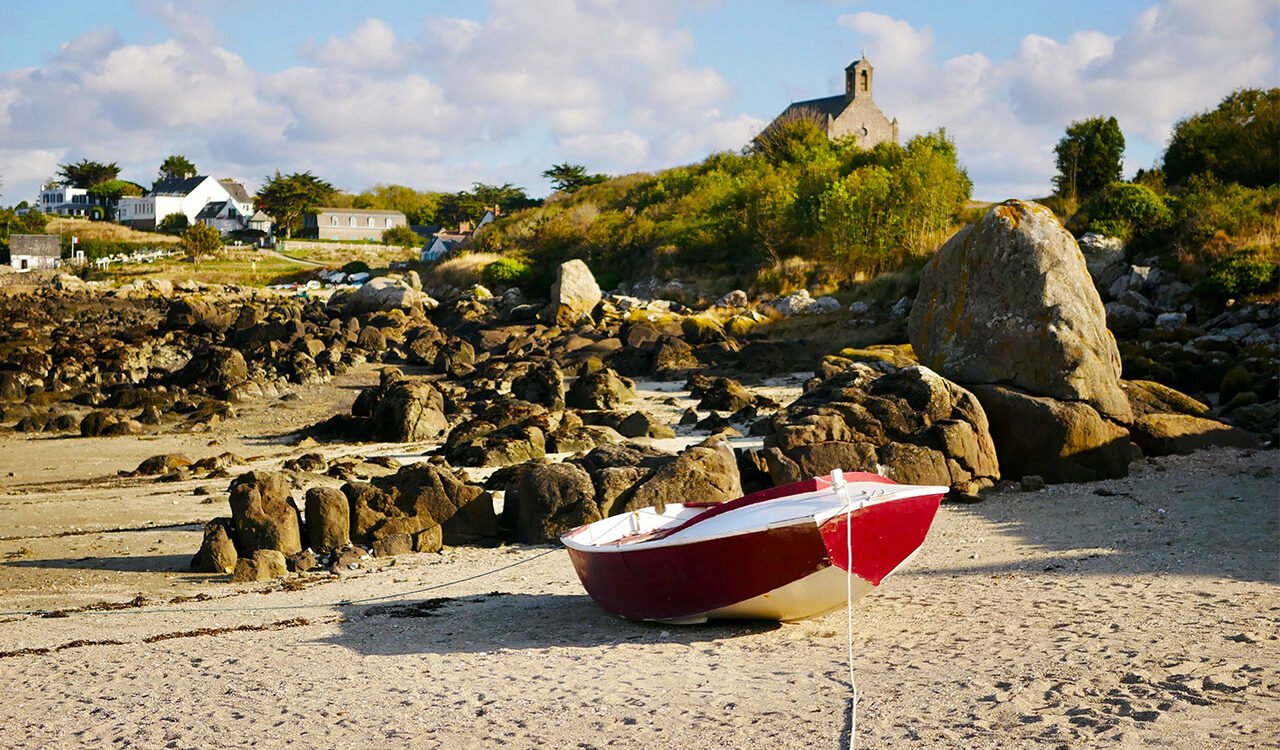 barque rouge posée sur le sable sur l'île principale de l'Archipel de Chausey. En arrière plan l'église et le tout petit village de Chausey.