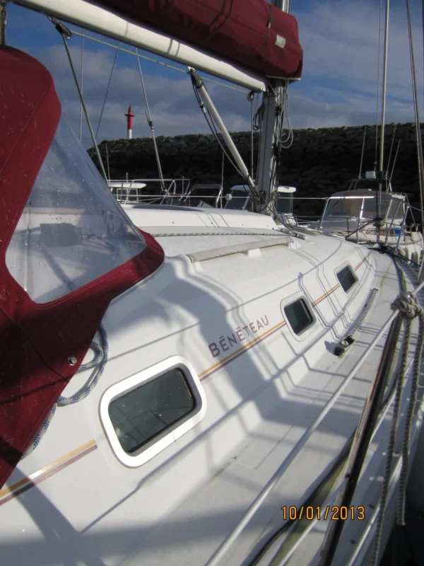 Proue d'un bateau à voiles au port avec une balise d'entrée de port en fond. Un bénéteau de type Oceanis 311 dériveur lesté