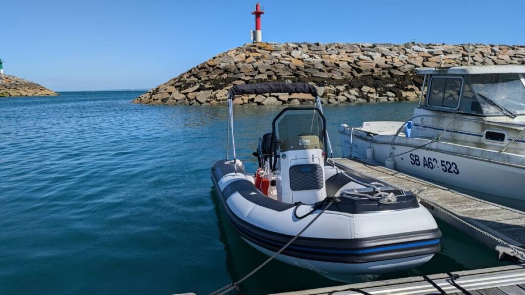 bateau moteur type zodiac amarré à un port avec une balise rouge en arrière plan.