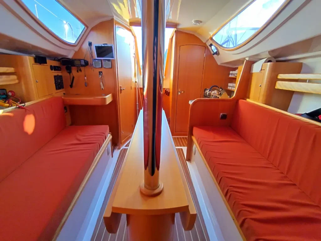 Vue intérieure du carré du Maxus 28 vers l’arrière, avec table à cartes rabattable, banquettes en tissu gris, boiseries claires, hublots latéraux et descente vers la cabine arrière.